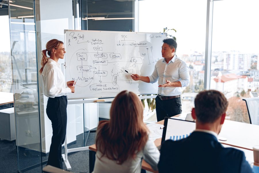Asian man and woman conducts a meeting for employees near the board and explains the work strategy.