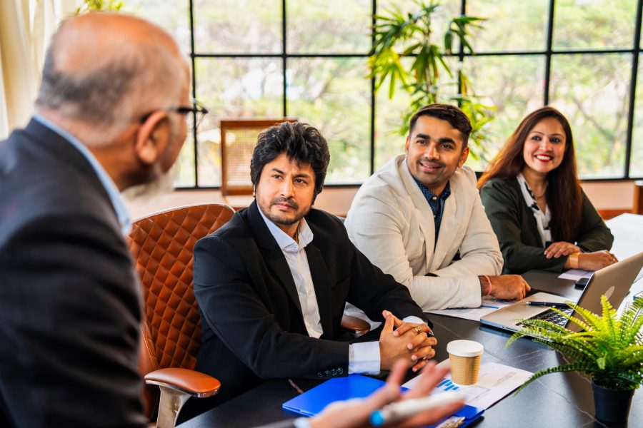 Indian Asian senior business professional or CEO presenting strategy on a glass board or delivering a motivational speech to his young team during a meeting in a corporate conference room