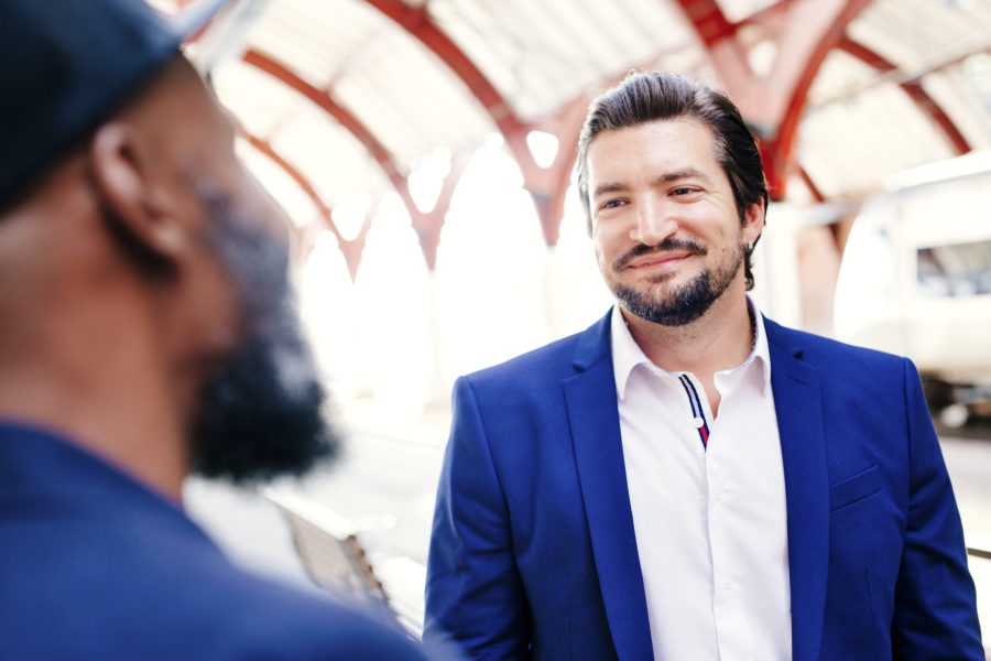 Smiling businessman standing with male colleague at railway station